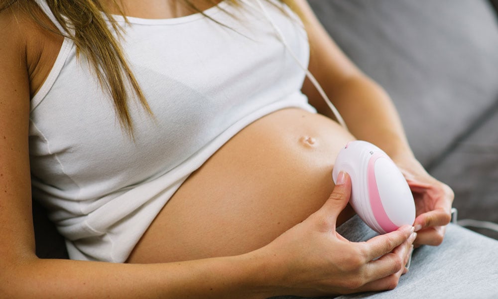 Voorbeeld van een zwangere vrouw die thuis een doppler gebruikt. Getty Images
