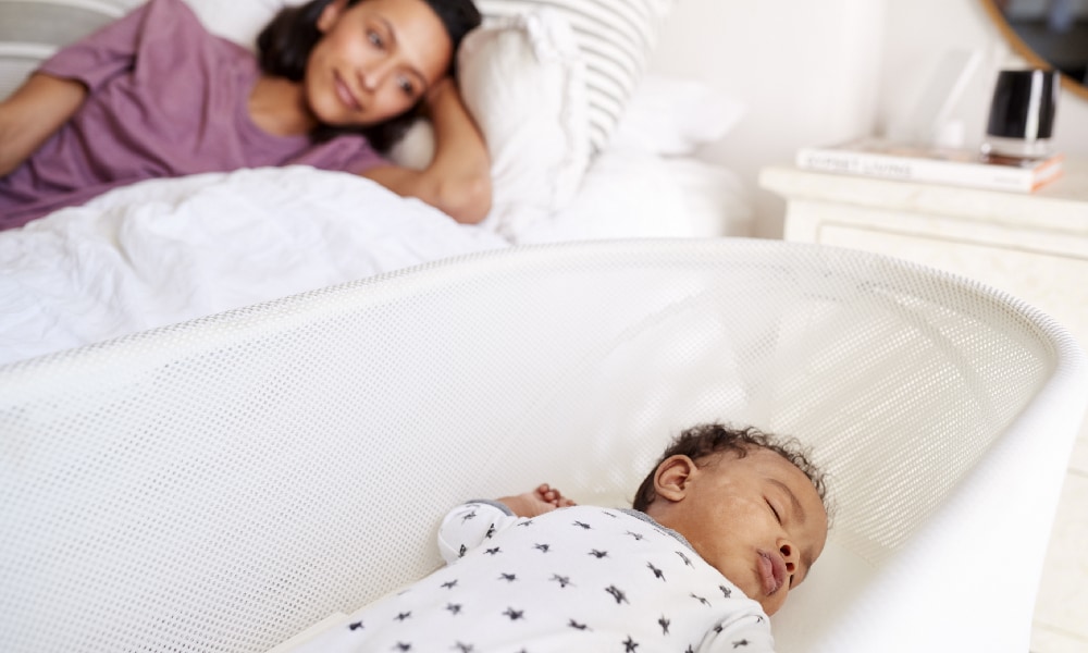 vrouw kijkt vanuit naar slapende baby in co-sleeper Getty Images