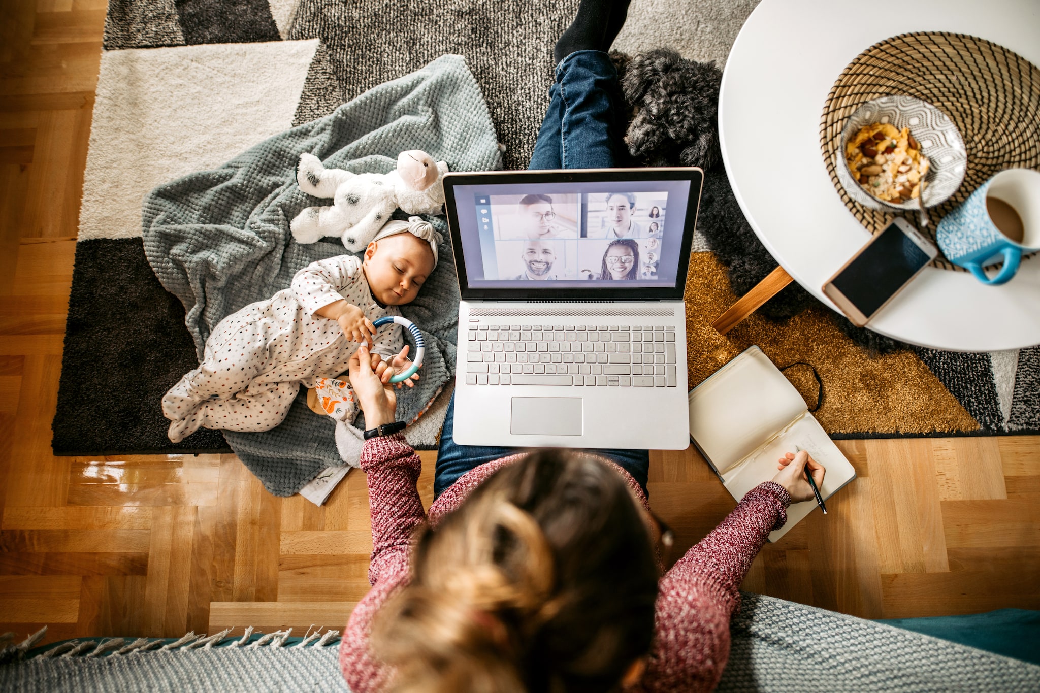 Cute little baby playing on the floor by her working mother.  Young mother with a baby and a dog, sitting on the floor and working. High angle of view. Getty Images