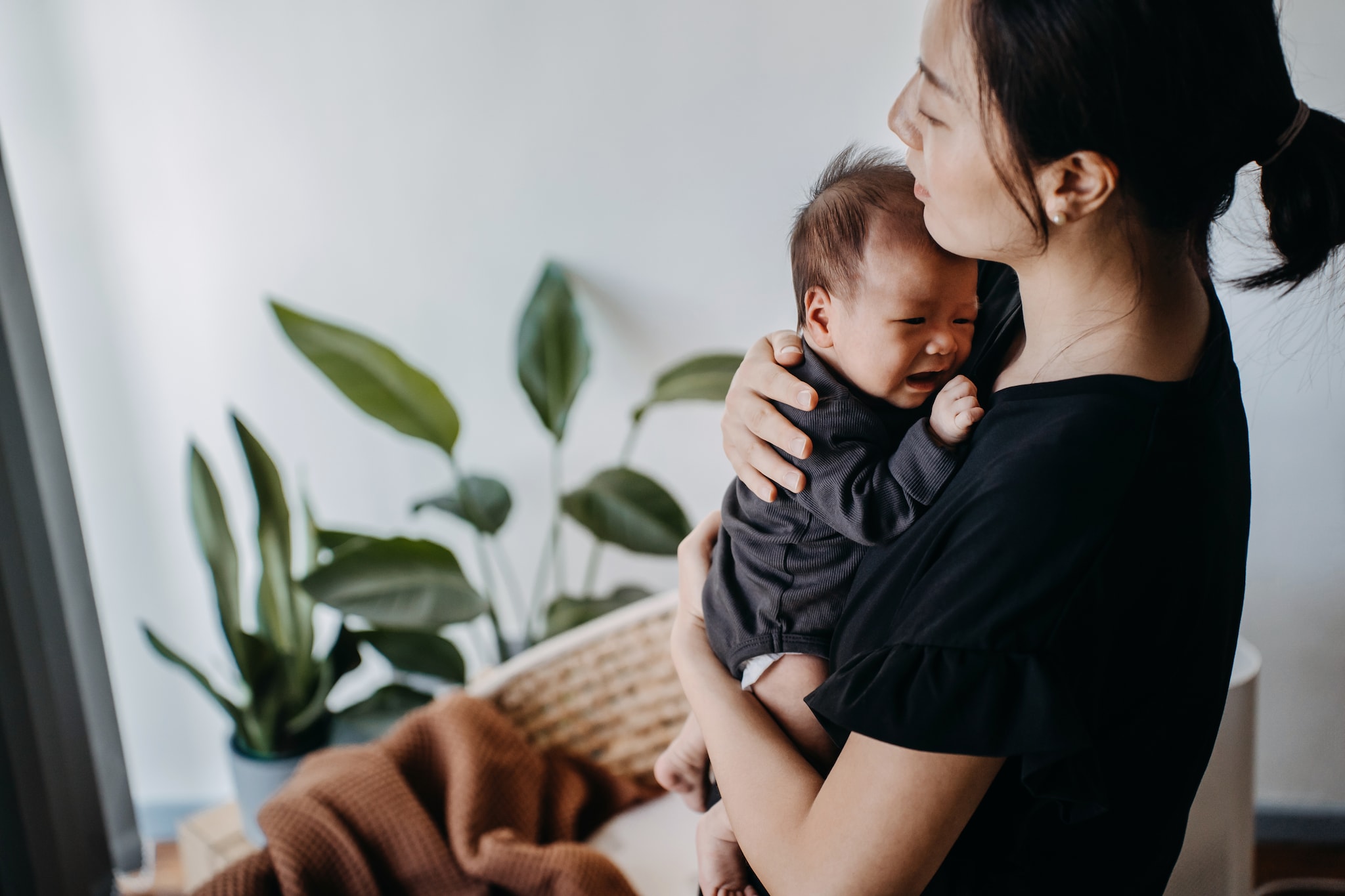A loving young Asian mother carrying her newborn baby girl in arms, consoling and comforting her crying baby. Hunger and discomfort. Love and care. Motherhood and parenthood concept Getty Images
