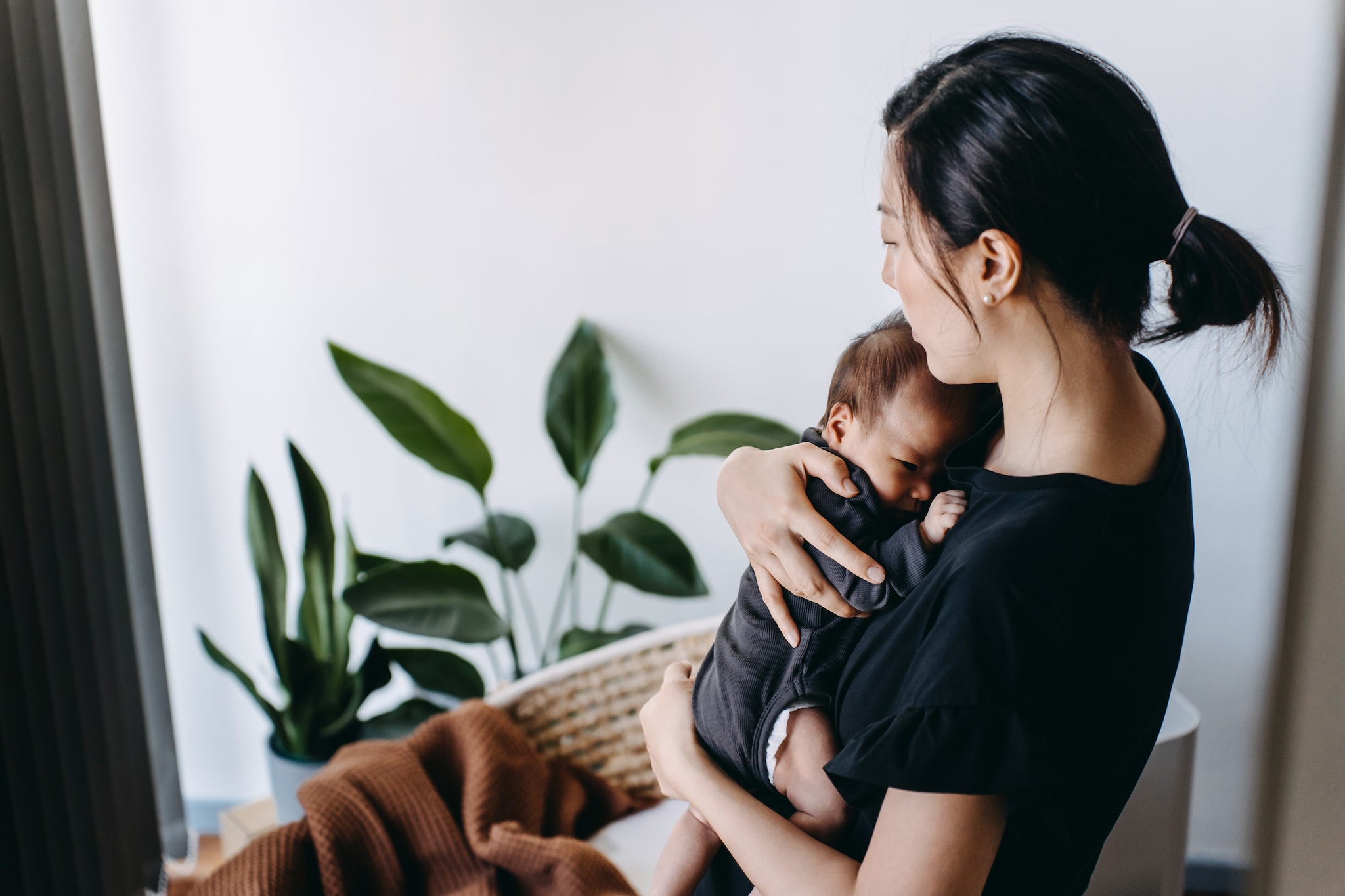 Loving young Asian mother carrying her newborn baby daughter in arms in the nursery, comforting and gently patting her to sleep. Love, care and tenderness. Motherhood, parenthood concept Getty Images