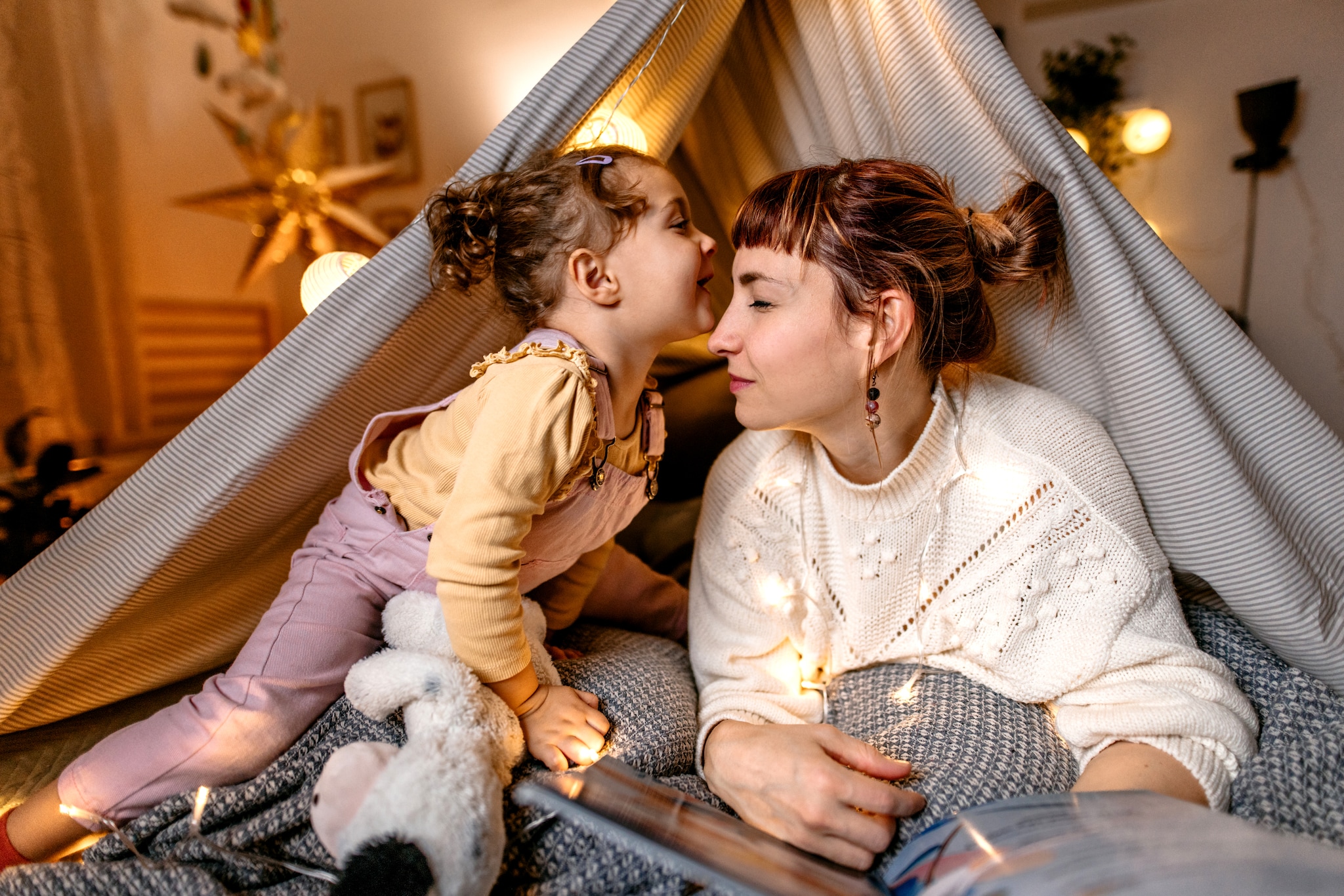 Mother and daughter are having fun reading a book under the illuminated tent in the bedroom. Getty Images