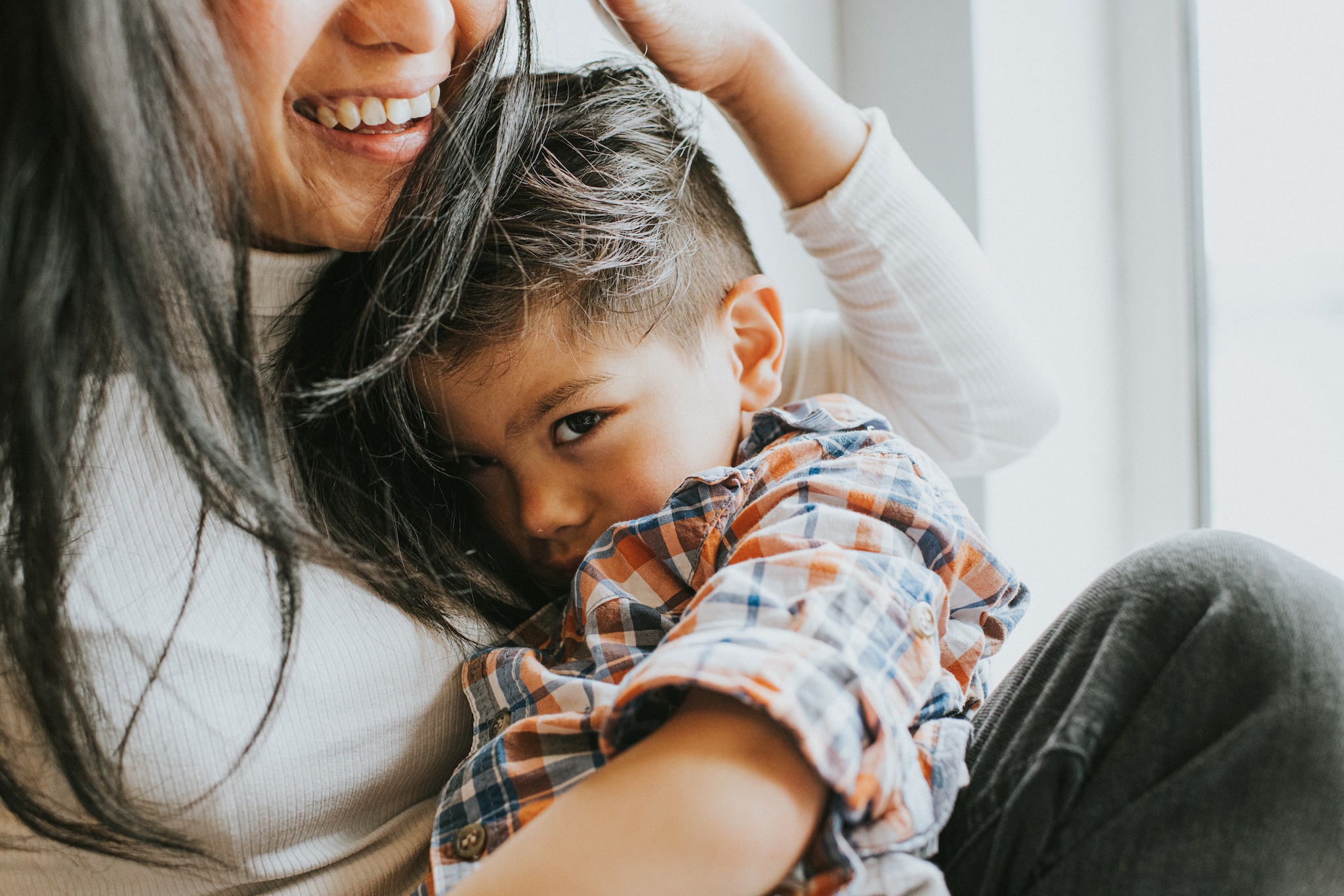A mother smiles as she cradles her cute young son, who shyly snuggles in to her and glances towards the camera, with uncertainty. Getty Images