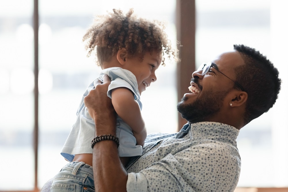 Happy daddy holding kid in arms, hugging toddler boy. African American dad enjoying being father, spending time and playing with cute preschooler son, talking to child, laughing. Parent concept Getty Images/iStockphoto