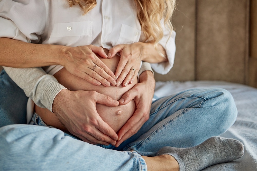Close up of couple making heart shape on woman's pregnant belly. Getty Images