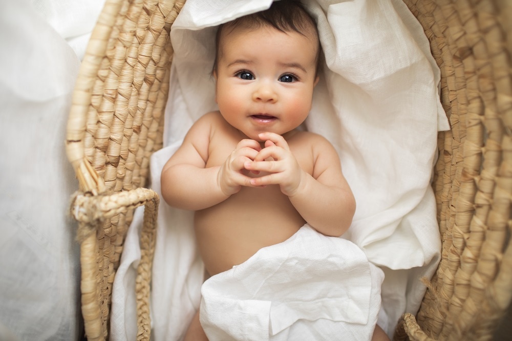 Adorable smiling beautiful baby girl lying in vintage baby wicker cot. Funny naked child in moses basket. Eco bedding for kids. Getty Images