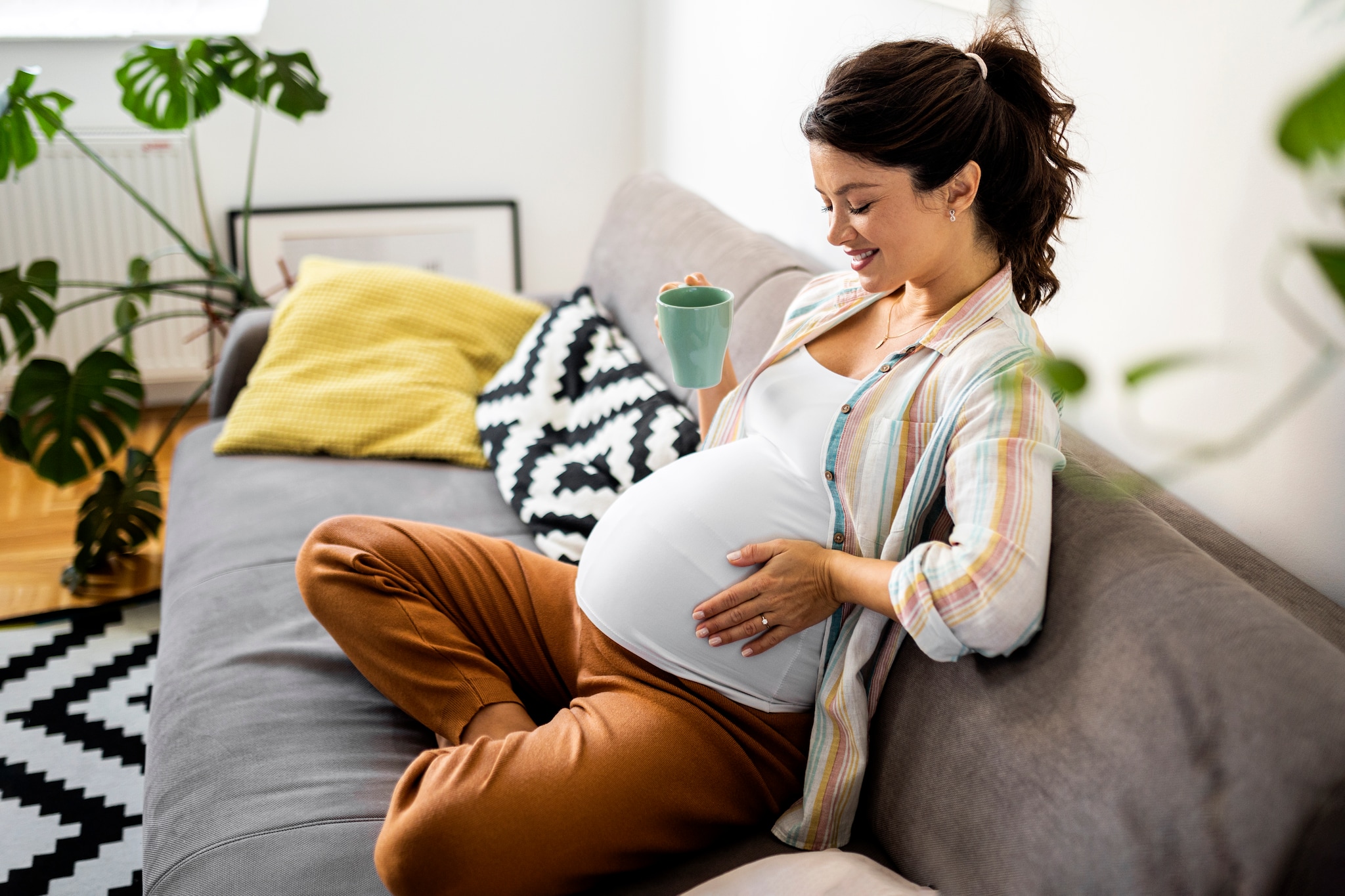 Pregnant woman resting on sofa holding cup of coffee Getty Images