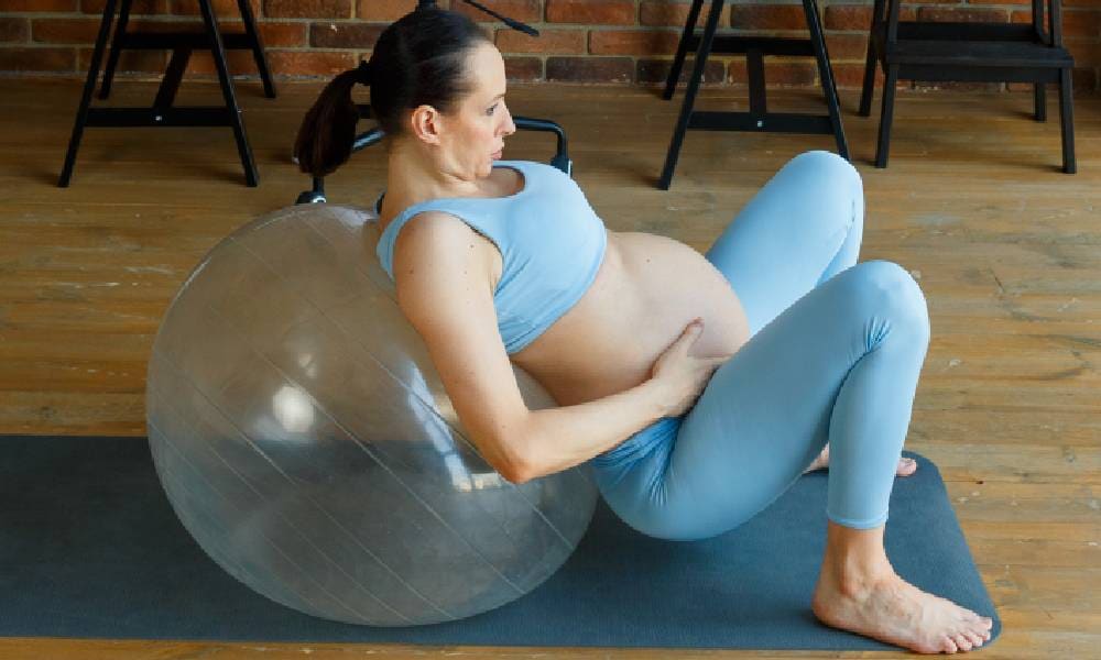 Zwangere vrouw hurkt tegen bevalbal aan Getty Images