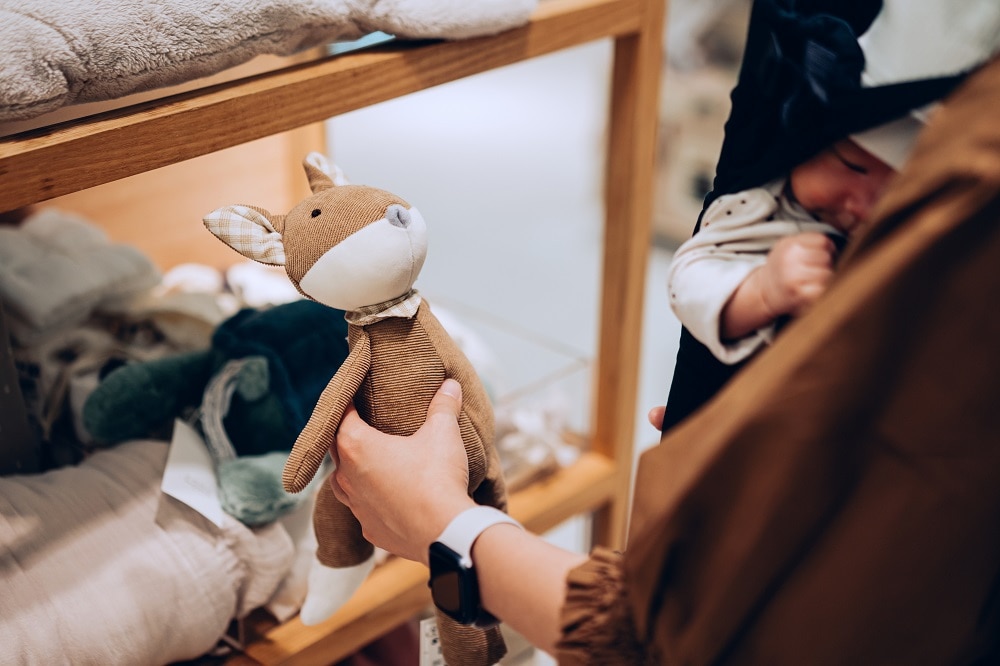 Cropped shot of young Asian mother carrying her baby girl in carrier, shopping for soft toys and baby essentials in a boutique. Mother shopping for kids products and essentials in a store Getty Images