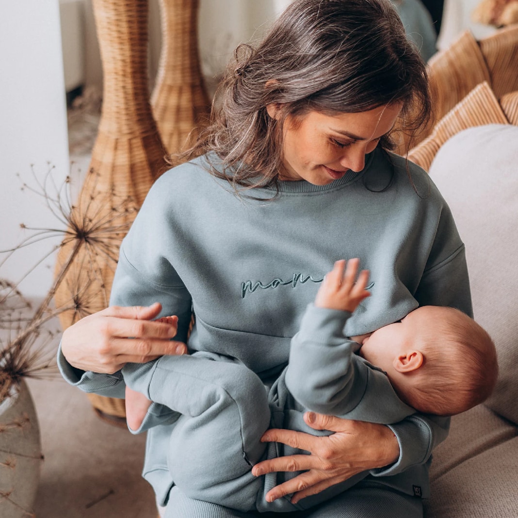 Vrouw voedt baby in blauwe borstvoedingsweater met 'mama' borduursel MyGang