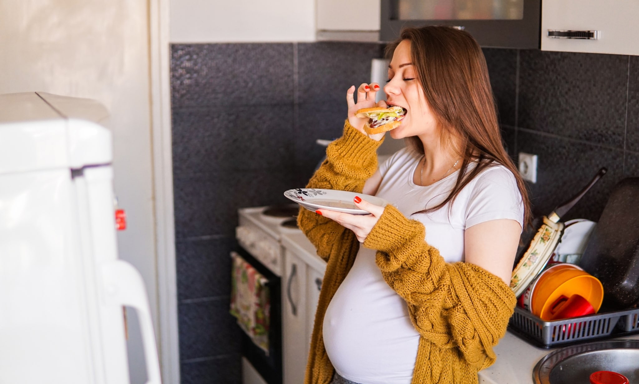 Zwangere vrouw etend in keuken, bij rubriek Kommer&amp;Kwaal over kaakgewrichtsklachten, Getty Images