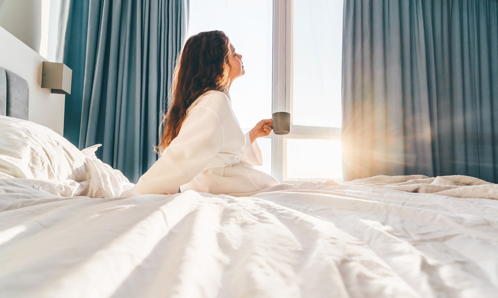 Vrouw ontspant in bed hotelkamer, bij artikel over kraamhotel. Getty Images