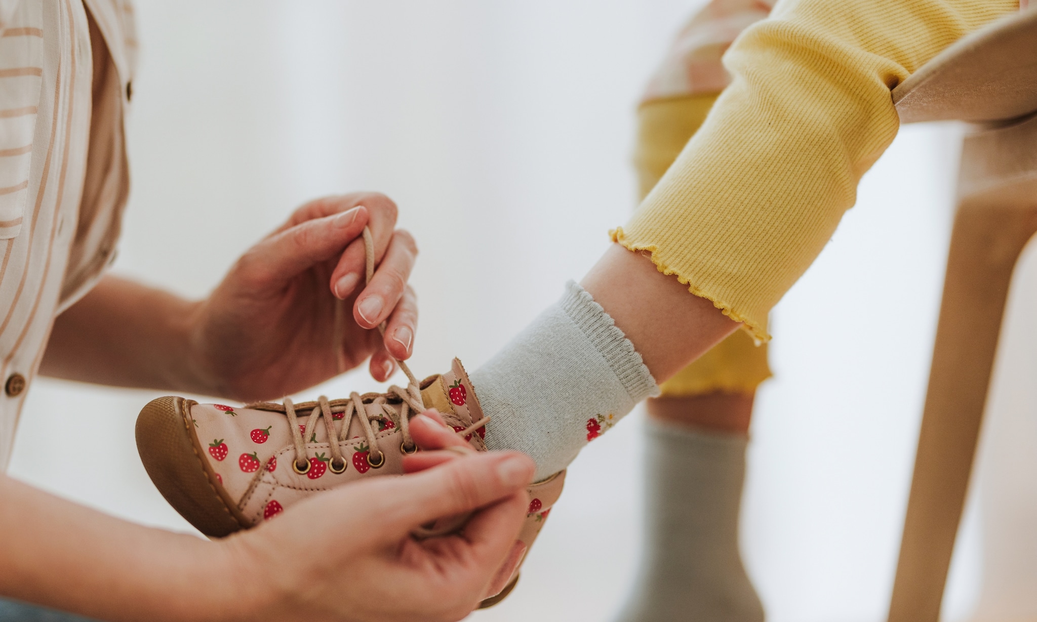 moeder meet juiste schoenmaat van kind en helpt met aantrekken kinderschoen voorjaar zomer Getty Images