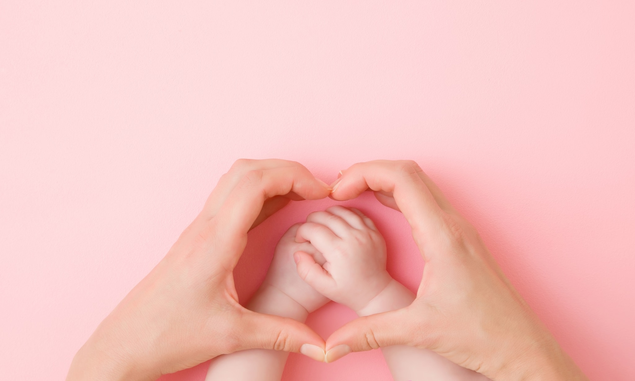 Handen van volwassene vormen hart boven handen van baby, bij rubriek Alleen verder. Getty Images