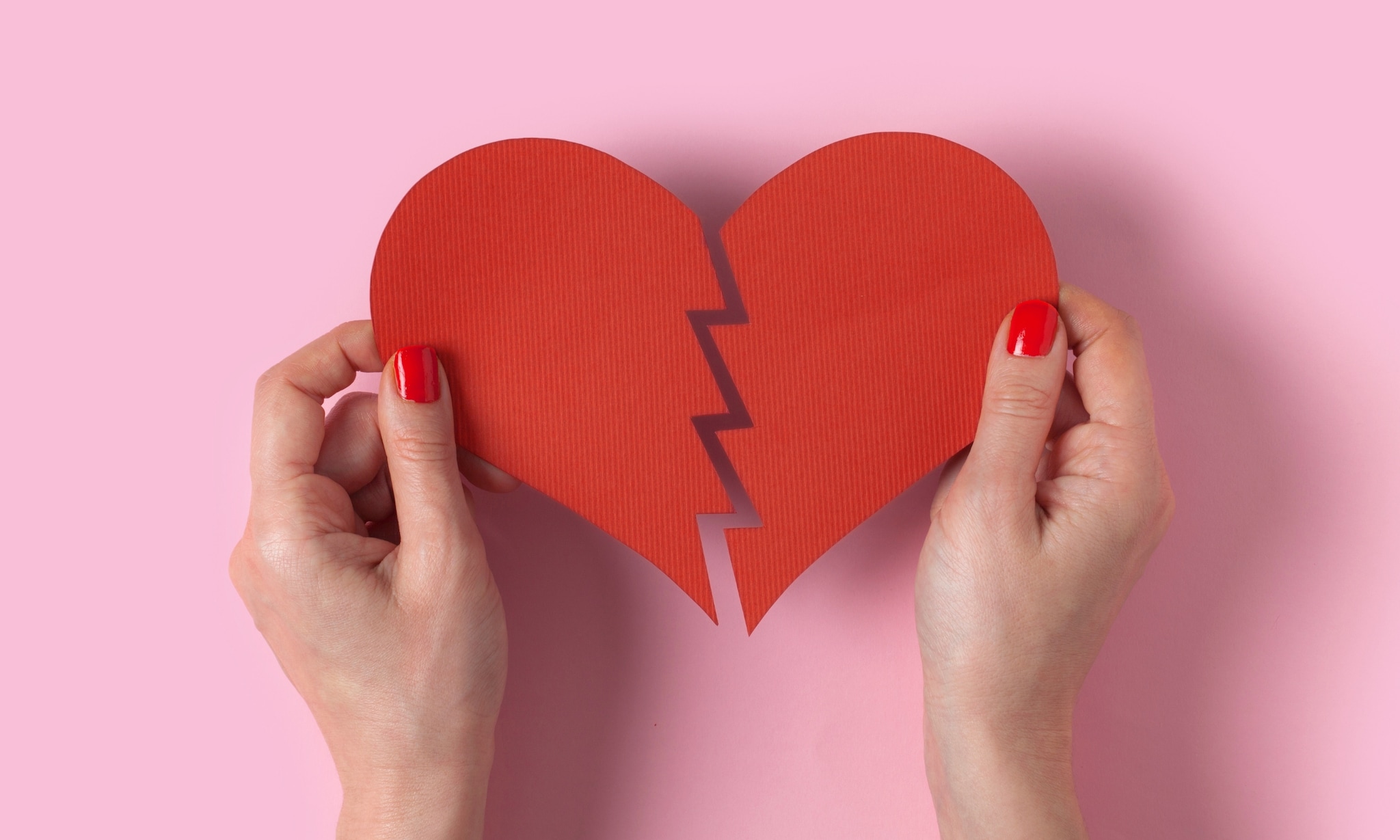 Handen met gebroken hart van papier op roze achtergrond, bij rubriek Alleen verder. Getty Images
