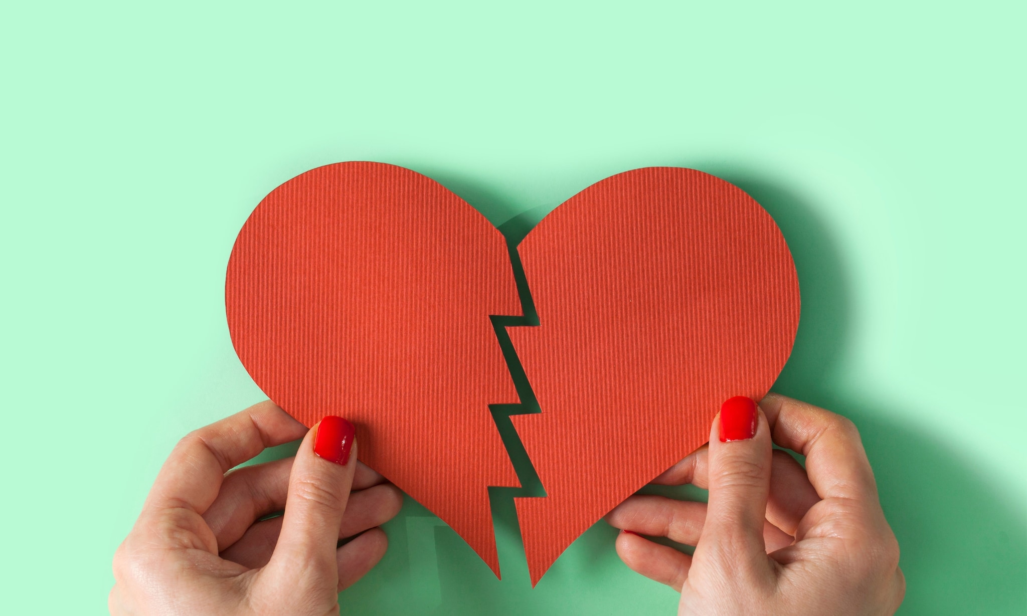 Handen met gebroken hart van papier op groene achtergrond, bij rubriek Alleen verder. Getty Images