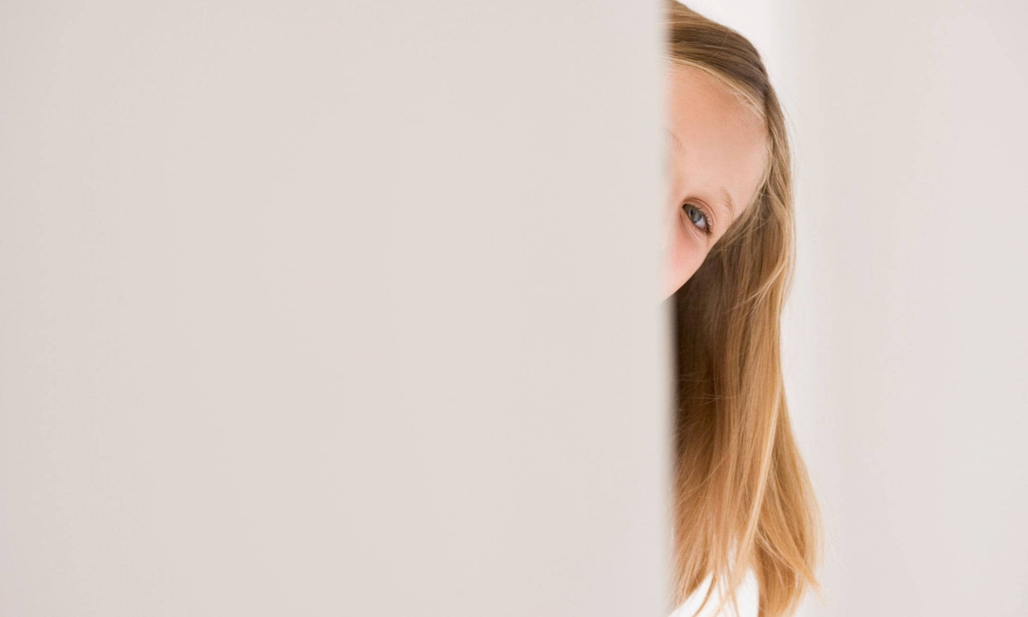 Meisje kijkt om het hoekje van een deur. Getty Images