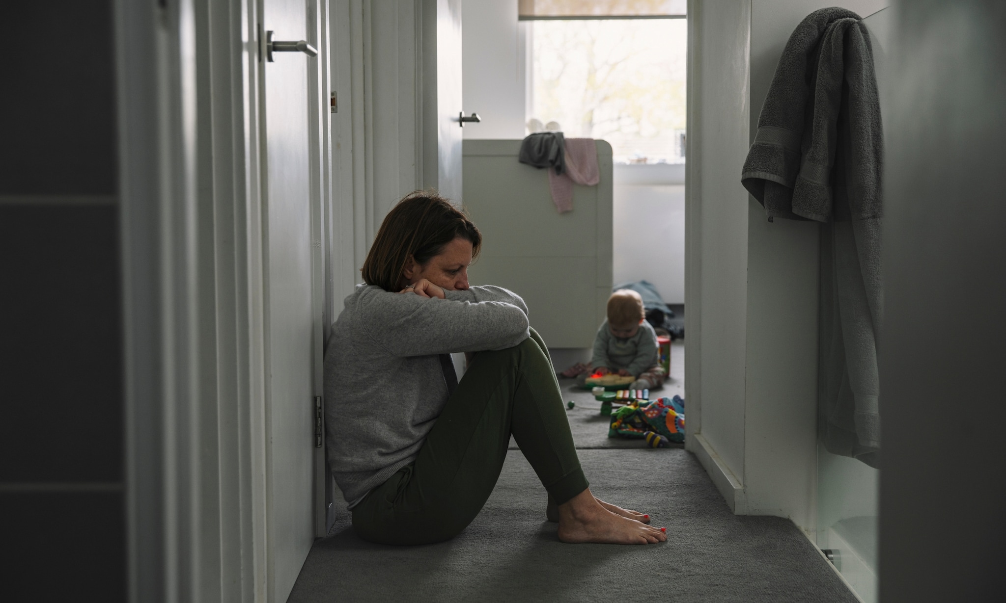 Spijtmoeder, moeder die peinzend op de grond zit bij kind dat alleen speelt. Beeld is illustratief, dit is niet de moeder uit het verhaal. Getty Images