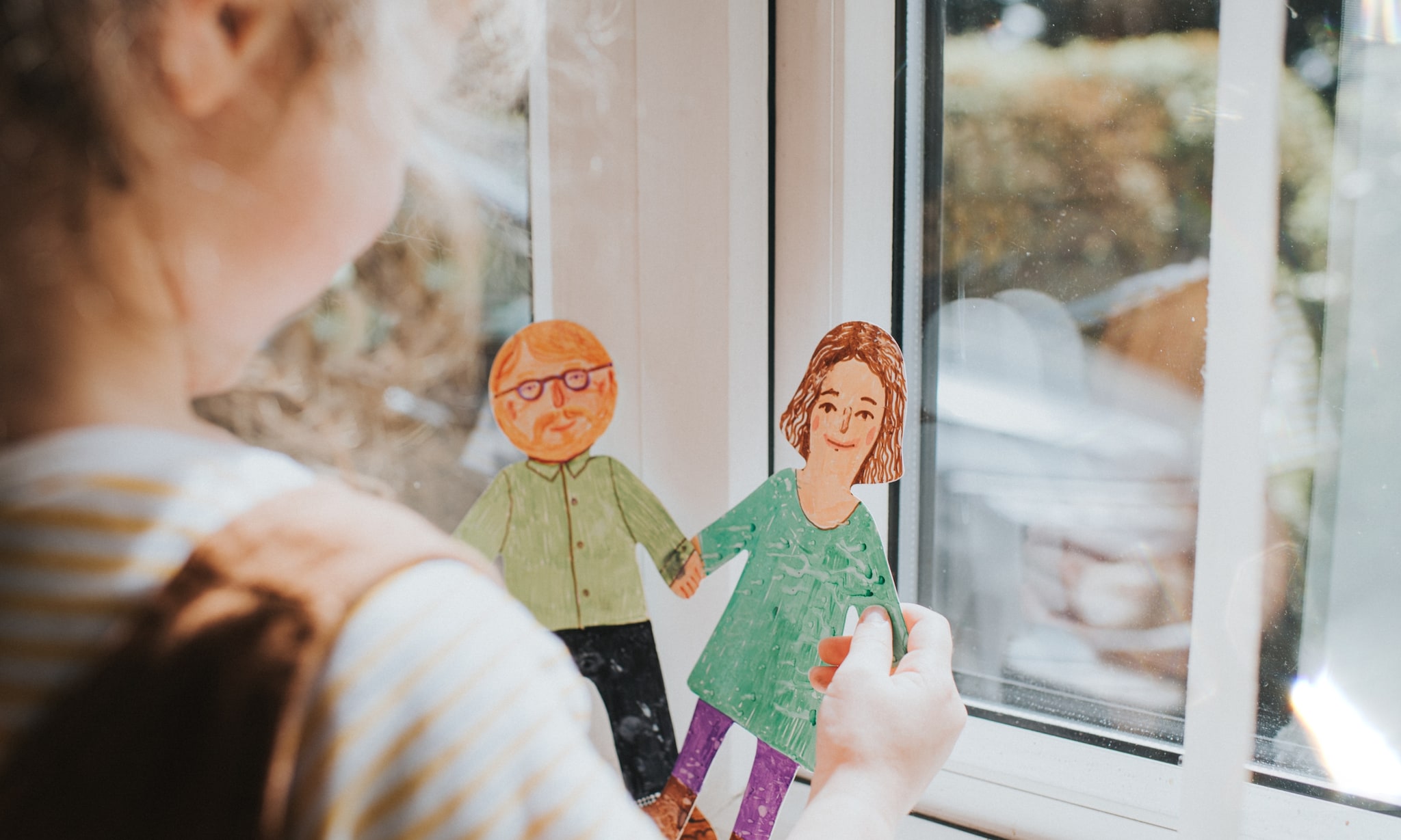 Meisje op de rug gezien bij een raam, speelt met getekende man en vrouw, bij artikel over pleegouders. Getty Images