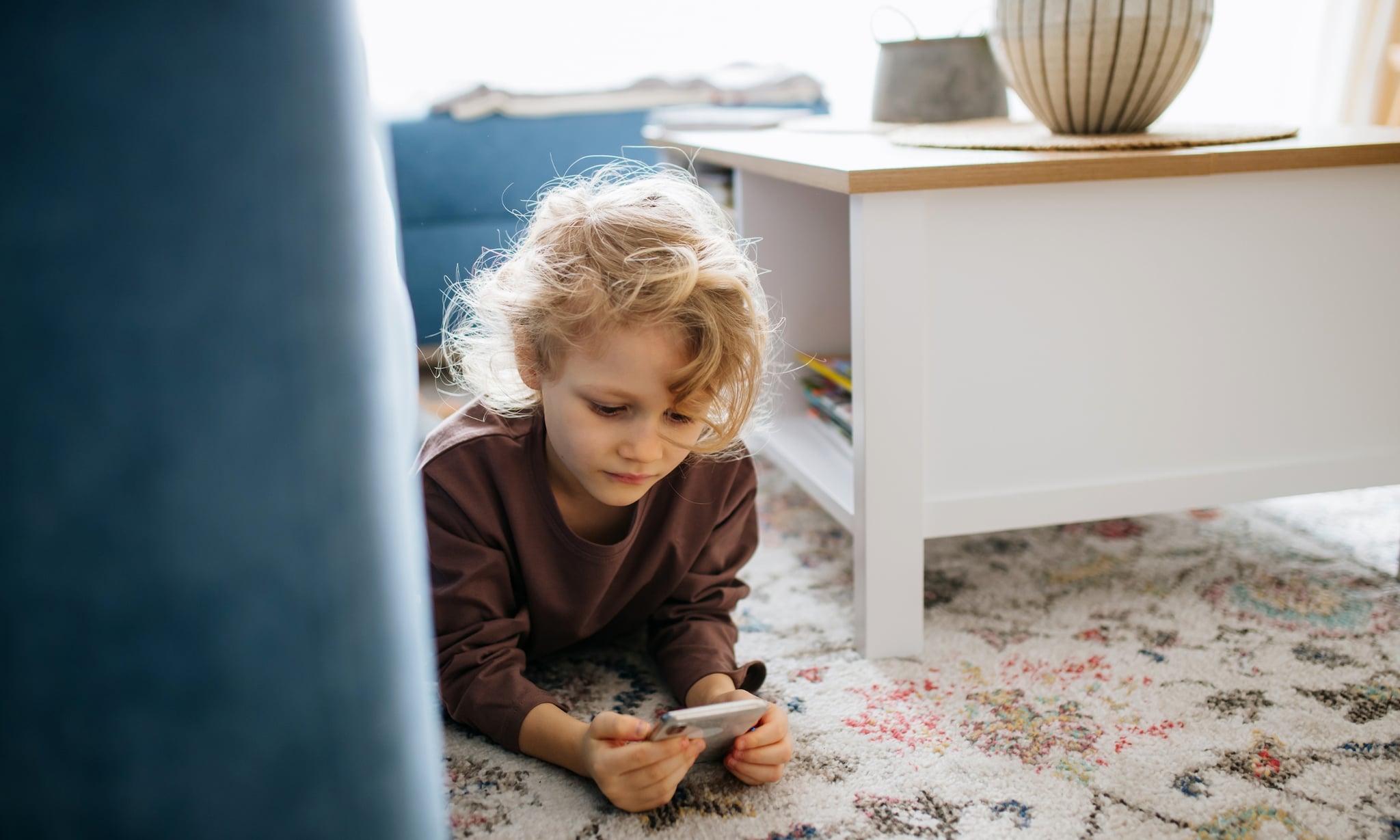 Meisje met smartphone liggend op kleed in woonkamer. Getty Images