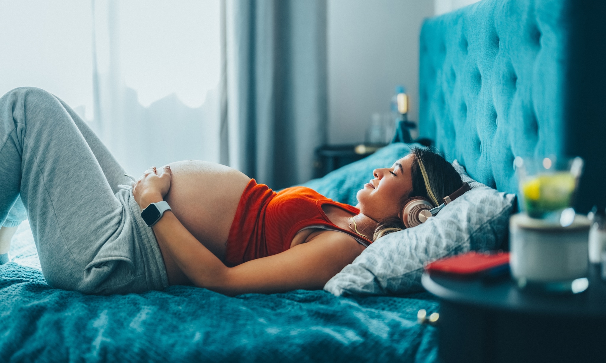 Zwangere vrouw liggend op bed luistert naar podcast. Getty Images