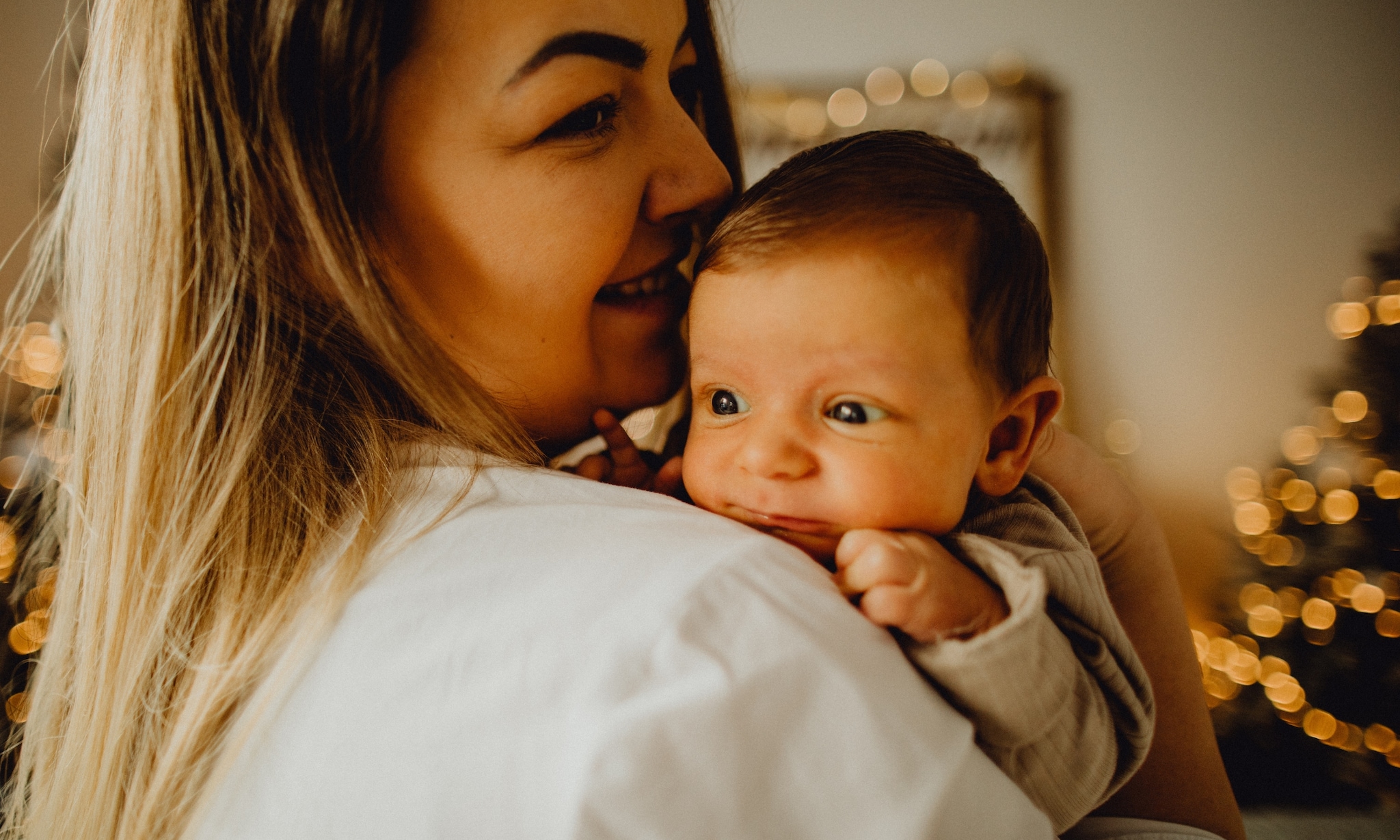 moeder staat voor kerstboom en houdt baby vast, dit zijn leuke kraamcadeaus als je rond de kerst uitgerekend bent Getty Images
