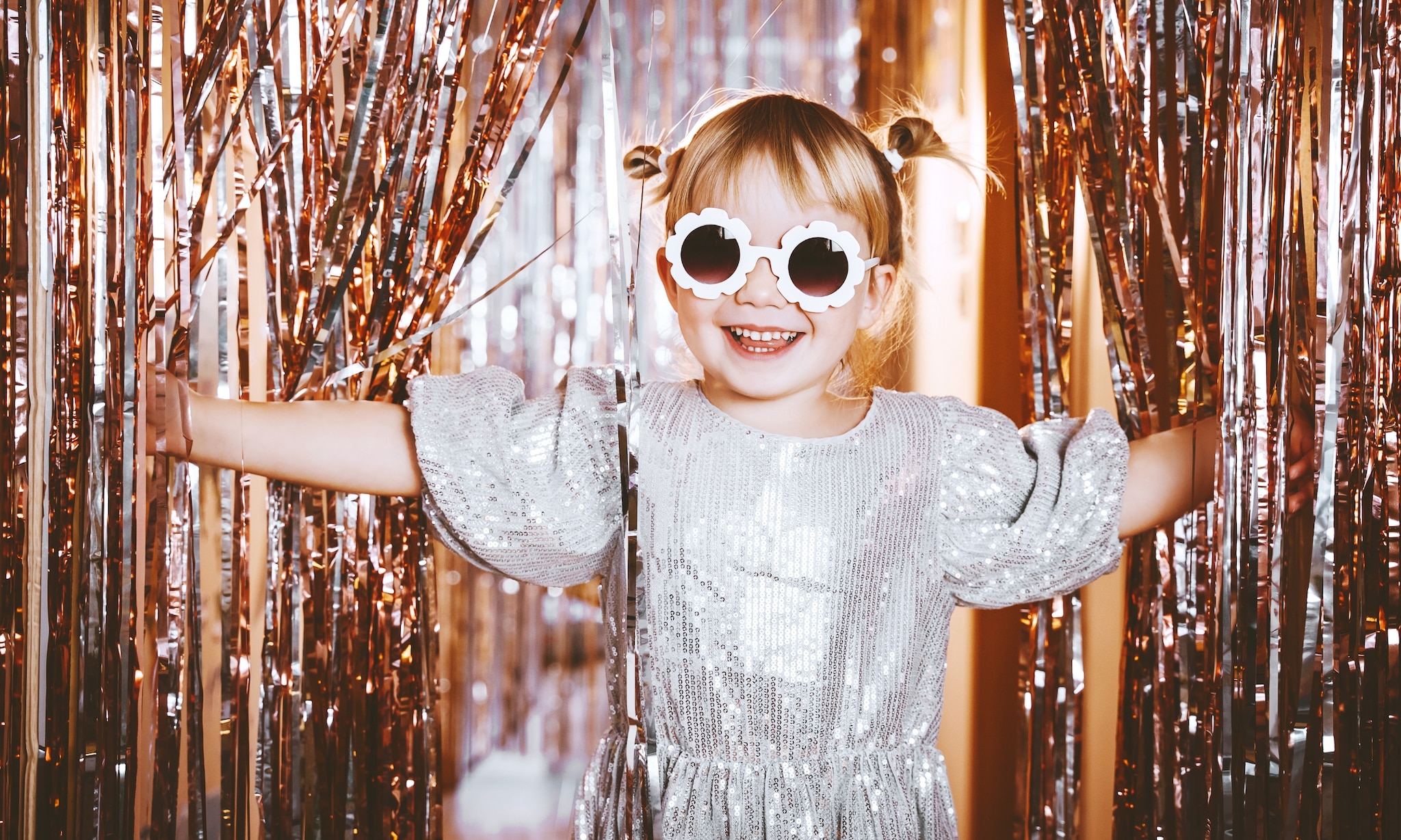 meisje in glitterjurk voor gouden glittergordijn, dit zijn de leukste ideeen om oud en nieuw met kinderen te vieren Getty Images