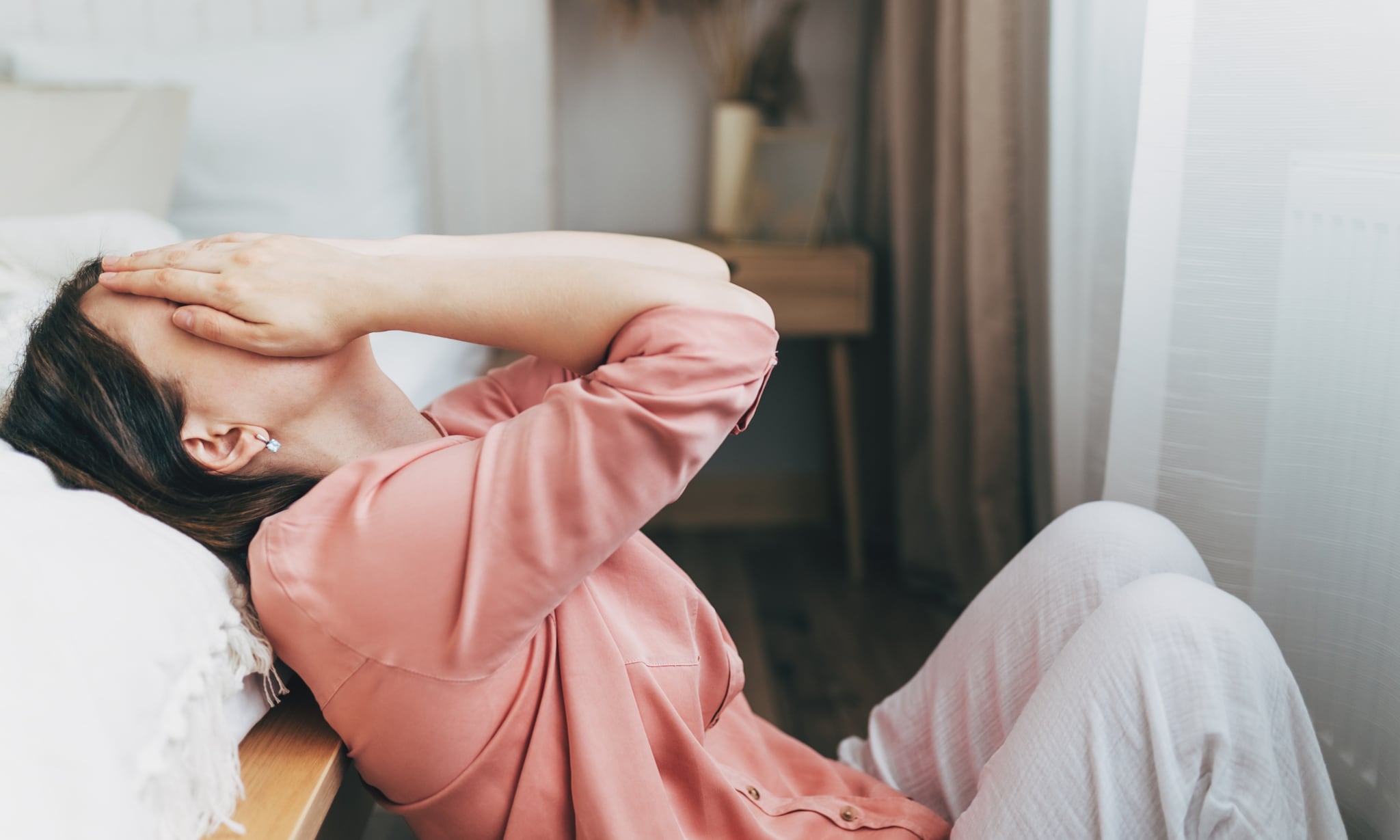 Vrouw op de grond naast bed, met handen voor het gezicht. Getty Images