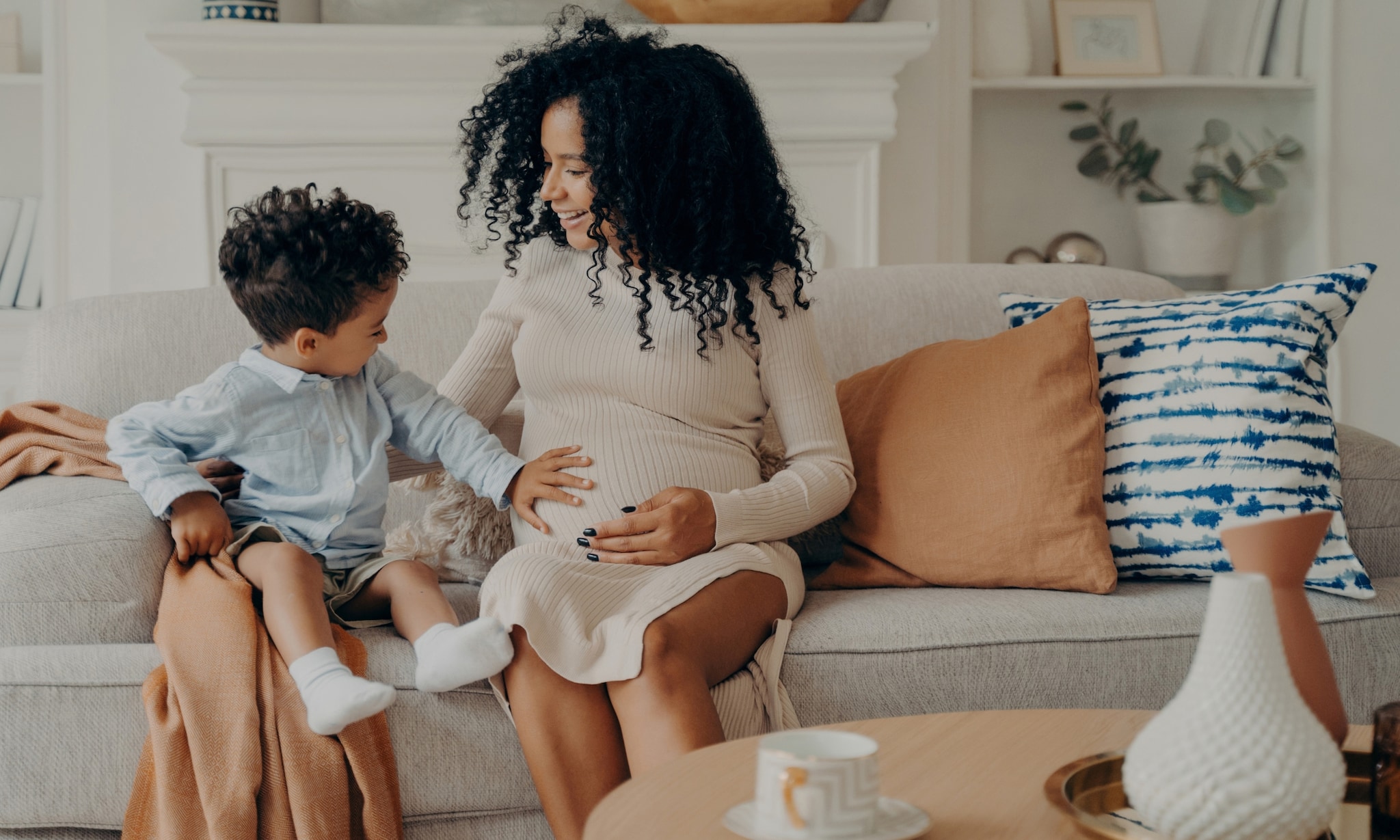 Vrouw draagt mooie zwangerschapsjurk en zoontje voelt aan haar buik. Deze zwangerschapskleding heb je wel en niet nodig Adobe Stock